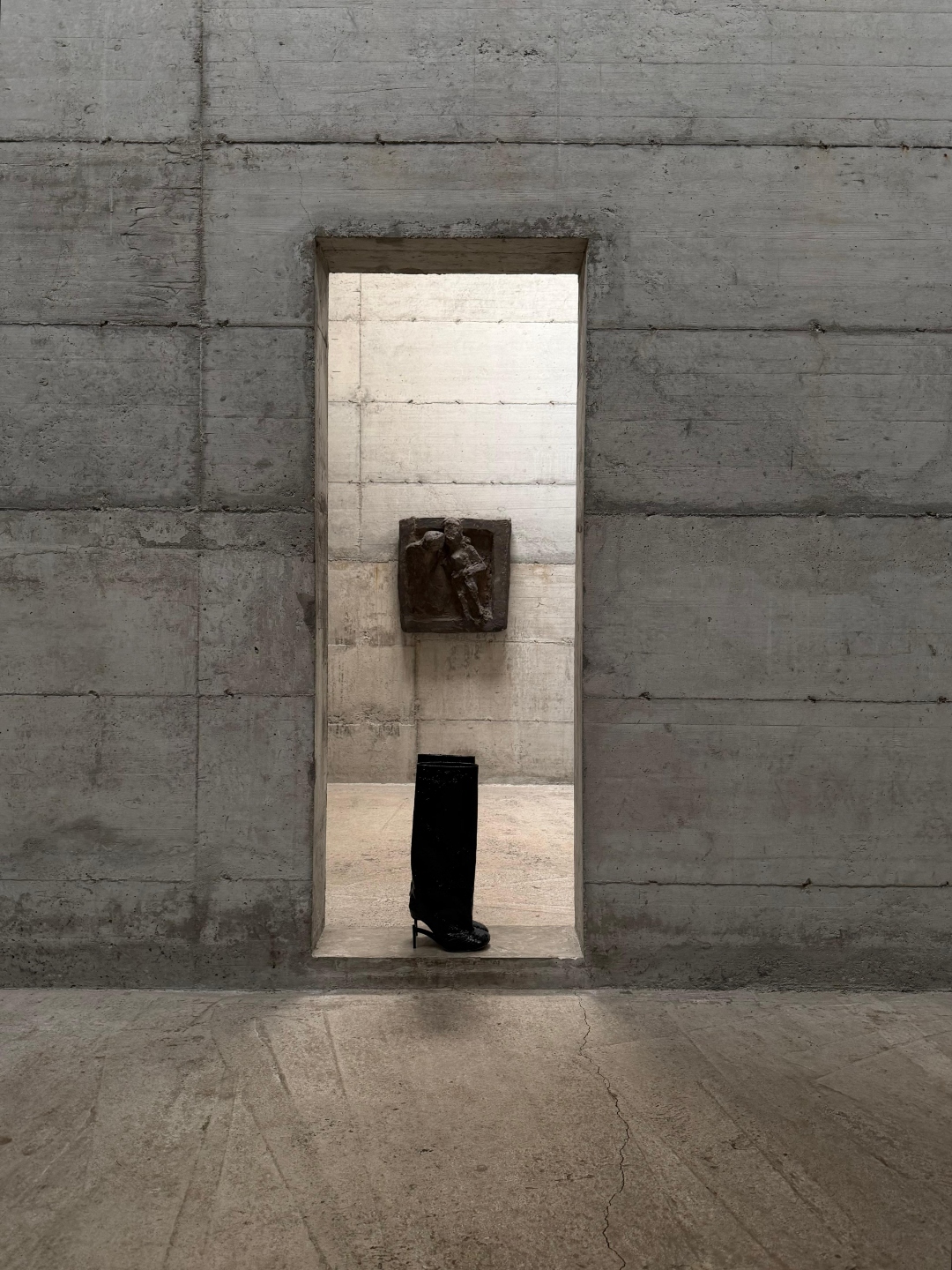A single boot in a vertical concrete niche, bronze relief above.